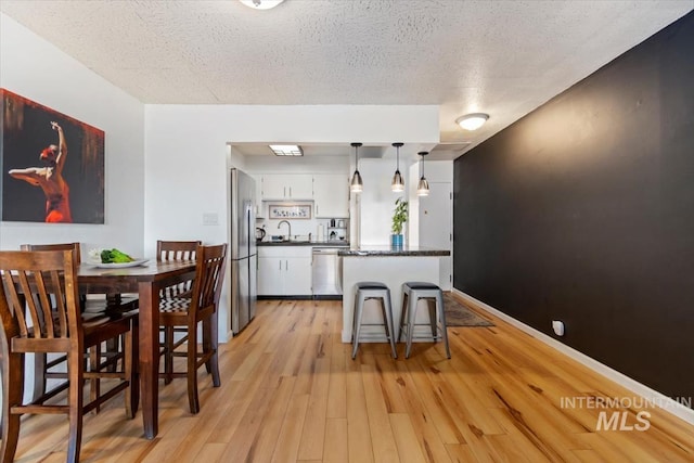 kitchen with light wood finished floors, stainless steel appliances, dark countertops, white cabinetry, and a textured ceiling