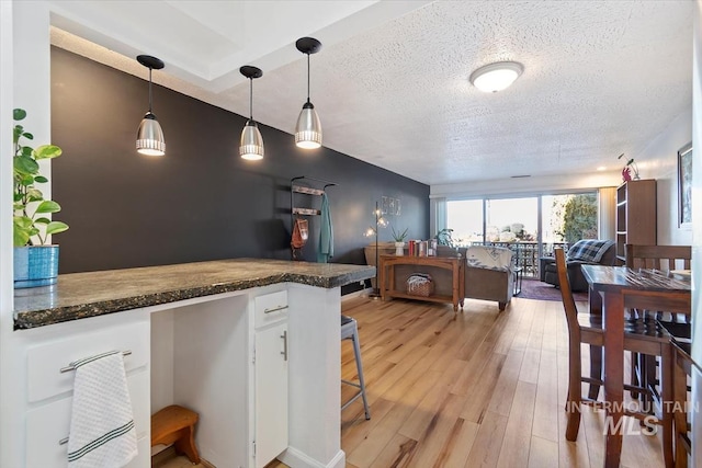 kitchen with a textured ceiling, white cabinets, open floor plan, light wood finished floors, and decorative light fixtures