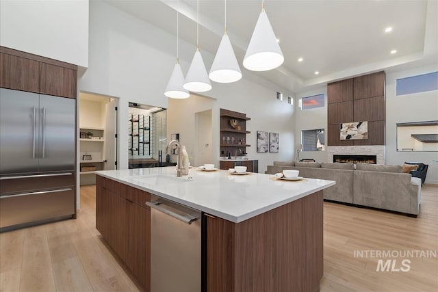 9891 W Napier Ct, Star, ID 83669 - kitchen featuring appliances with stainless steel finishes, a towering ceiling, modern cabinets, light wood-style flooring, and a fireplace