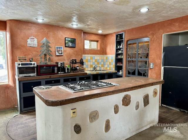 kitchen featuring sink, black refrigerator, dark hardwood / wood-style floors, tasteful backsplash, and stainless steel gas cooktop