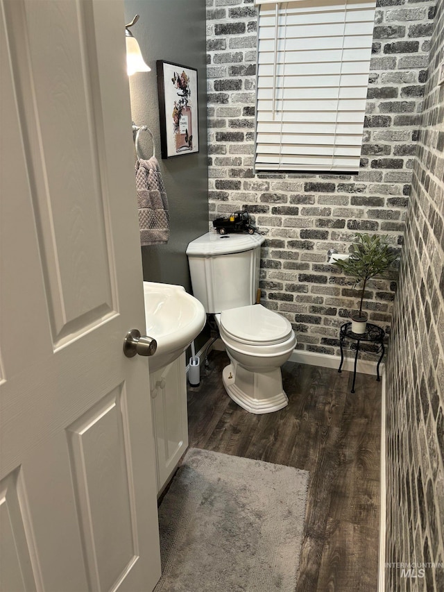 bathroom featuring sink, hardwood / wood-style floors, brick wall, and toilet