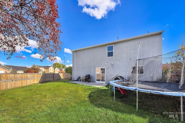 back of house featuring a yard, a patio, and a trampoline