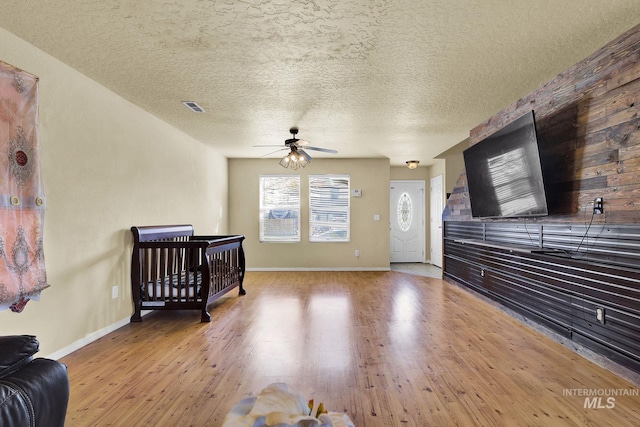 living room featuring ceiling fan, light hardwood / wood-style floors, and a textured ceiling