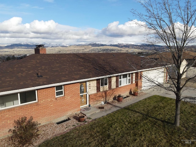 view of front of house with brick siding, a chimney, a front yard, and a mountain view