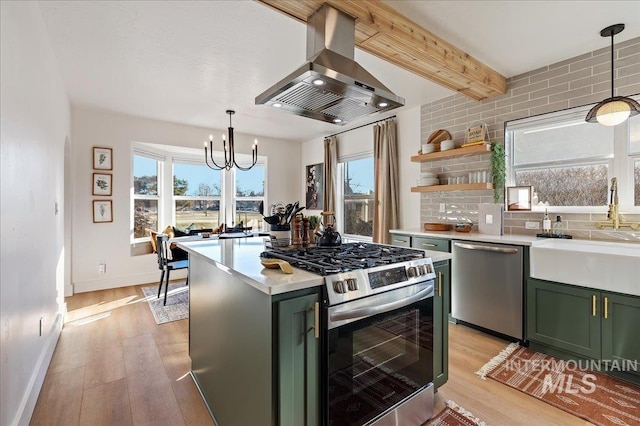 kitchen featuring green cabinetry, appliances with stainless steel finishes, decorative light fixtures, and island range hood