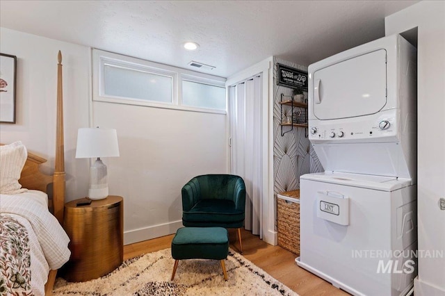 laundry area with stacked washer / dryer and light hardwood / wood-style flooring