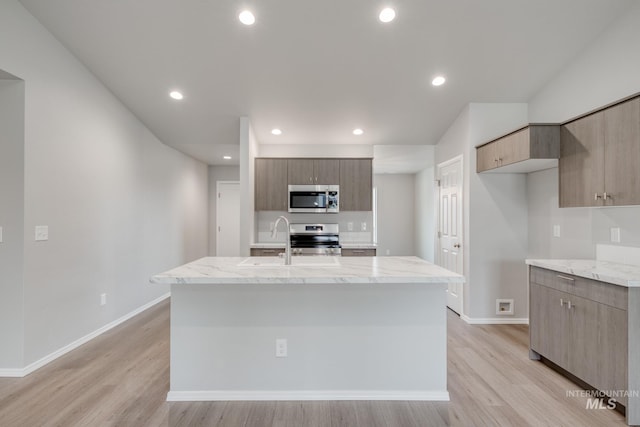 kitchen featuring sink, a kitchen island with sink, stainless steel appliances, light stone countertops, and light hardwood / wood-style flooring