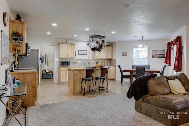 kitchen featuring a center island, light brown cabinets, decorative backsplash, a breakfast bar, and light tile patterned flooring