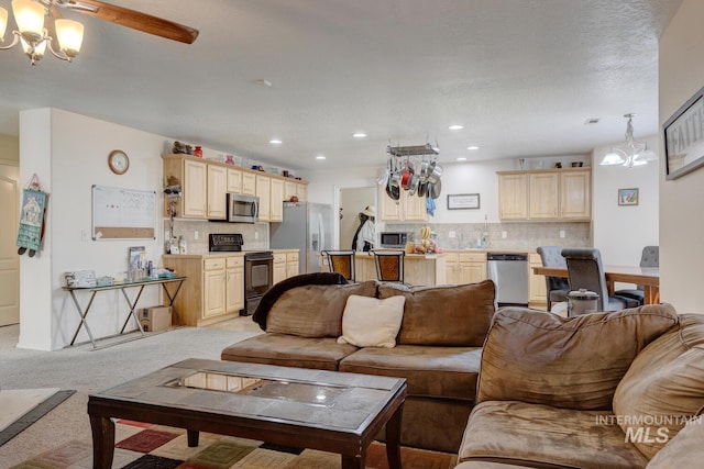 living room with ceiling fan with notable chandelier, light colored carpet, and a textured ceiling