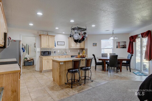 kitchen featuring a center island, hanging light fixtures, backsplash, light tile patterned floors, and appliances with stainless steel finishes