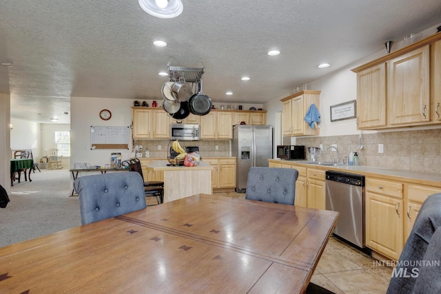 kitchen with backsplash, light carpet, a textured ceiling, light brown cabinetry, and appliances with stainless steel finishes