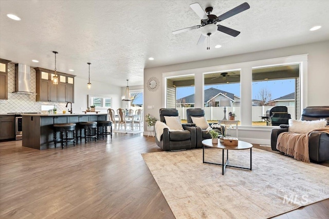 living room featuring ceiling fan with notable chandelier, hardwood / wood-style floors, and a textured ceiling