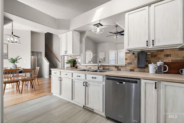 kitchen featuring light countertops, vaulted ceiling, a sink, dishwasher, and ceiling fan with notable chandelier