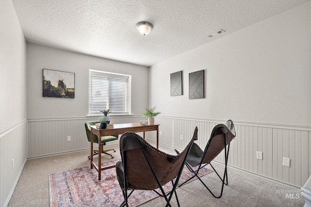 office area featuring a textured ceiling, visible vents, carpet flooring, and wainscoting