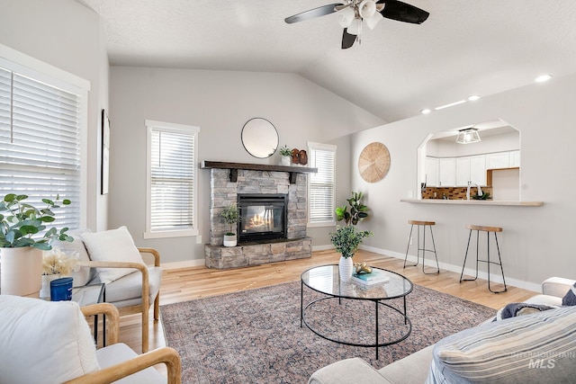 living area featuring lofted ceiling, ceiling fan, a fireplace, wood finished floors, and baseboards