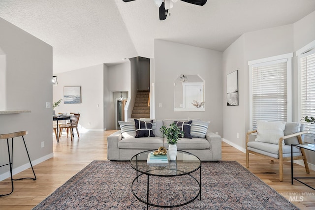 living area featuring light wood finished floors, lofted ceiling, a ceiling fan, a textured ceiling, and stairs