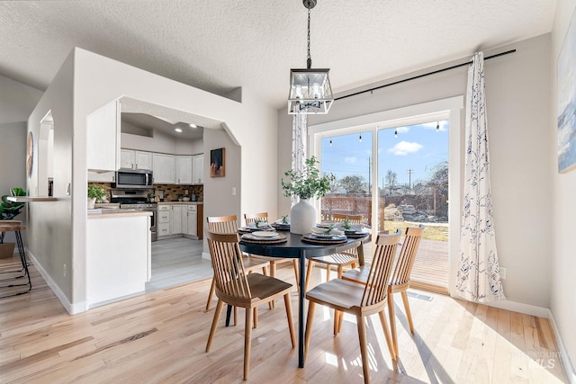 dining area with a chandelier, arched walkways, light wood-style flooring, and baseboards