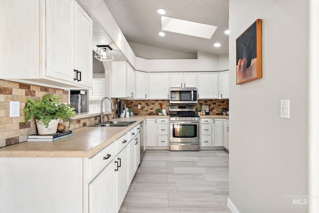 kitchen with a skylight, white cabinetry, appliances with stainless steel finishes, and a sink