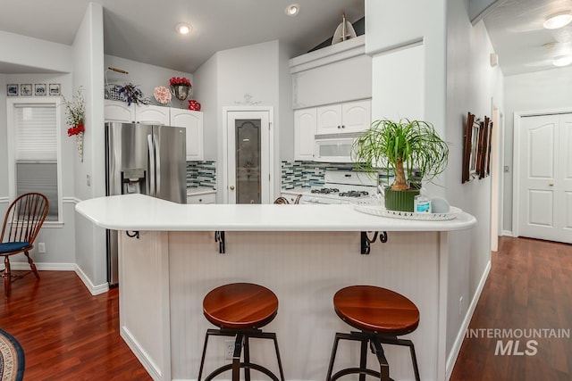 kitchen featuring white appliances, dark wood-style floors, a peninsula, white cabinetry, and tasteful backsplash