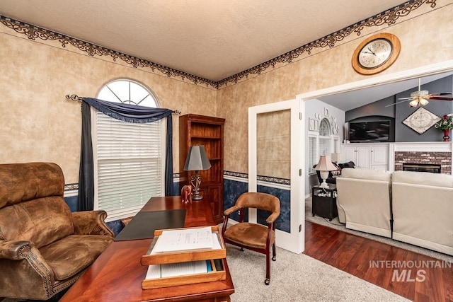 interior space featuring wood finished floors, lofted ceiling, ceiling fan, a textured ceiling, and a glass covered fireplace