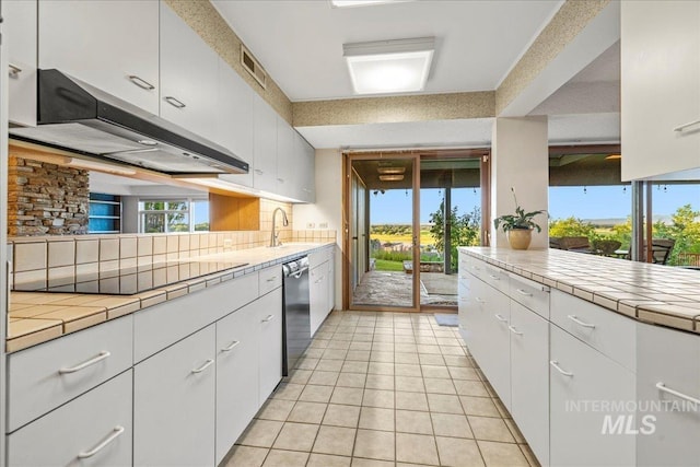 2401 Terrace Dr, Caldwell, ID 83605 - kitchen with black electric cooktop, tile counters, dishwashing machine, under cabinet range hood, and white cabinets