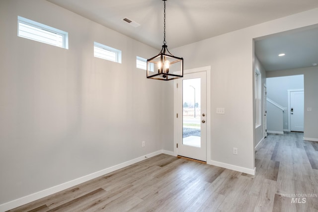 interior space with baseboards, an inviting chandelier, light wood-style flooring, and visible vents