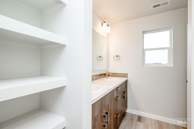 full bath with a sink, wood finished floors, visible vents, double vanity, and baseboards