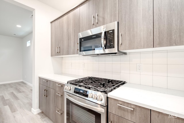 kitchen featuring light wood finished floors, stainless steel appliances, baseboards, light countertops, and tasteful backsplash