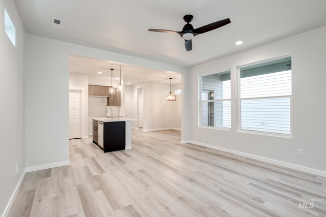 unfurnished living room with ceiling fan with notable chandelier, a sink, light wood-type flooring, baseboards, and recessed lighting