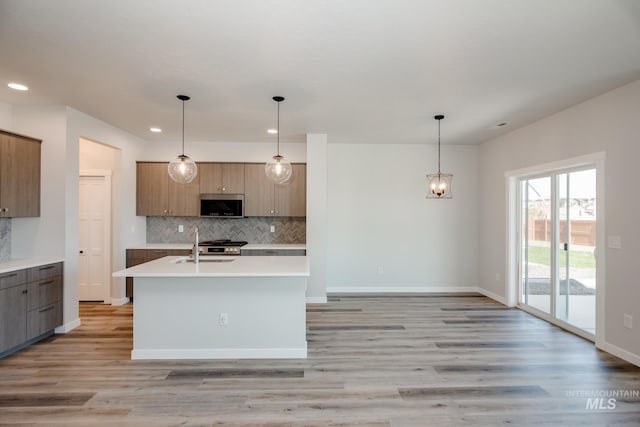 kitchen with light wood-style flooring, stainless steel microwave, light countertops, and decorative light fixtures