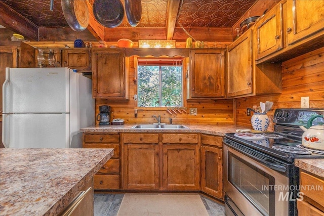 kitchen with an ornate ceiling, a sink, electric range, wood walls, and freestanding refrigerator