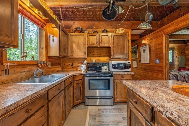 kitchen with a sink, white microwave, brown cabinets, stainless steel range with electric stovetop, and wooden walls
