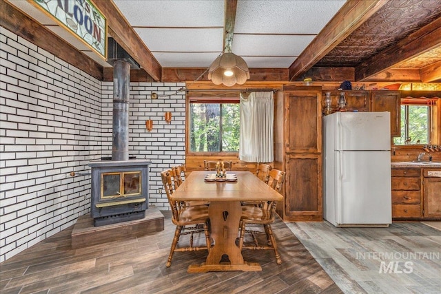 dining room with brick wall, wood finished floors, beam ceiling, and a wood stove