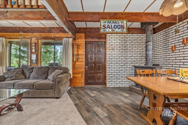 living area featuring dark wood-style flooring, beamed ceiling, brick wall, wooden walls, and a wood stove