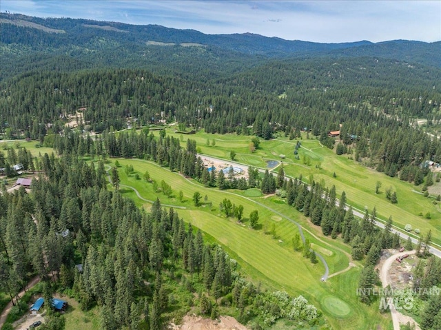 drone / aerial view featuring view of golf course, a mountain view, and a view of trees