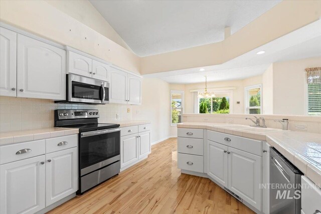 3314 S Raintree, Nampa, ID 83669 - kitchen featuring stainless steel appliances, tile countertops, light wood-style floors, white cabinets, and decorative backsplash