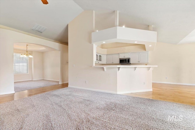 3314 S Raintree, Nampa, ID 83669 - unfurnished living room featuring lofted ceiling, a chandelier, light colored carpet, arched walkways, and light wood-type flooring