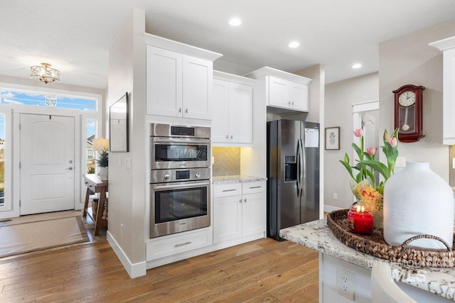 kitchen with stainless steel appliances, light wood-type flooring, white cabinets, and backsplash