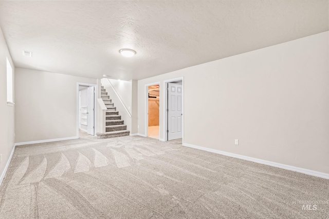 finished basement with visible vents, a textured ceiling, carpet flooring, baseboards, and stairs