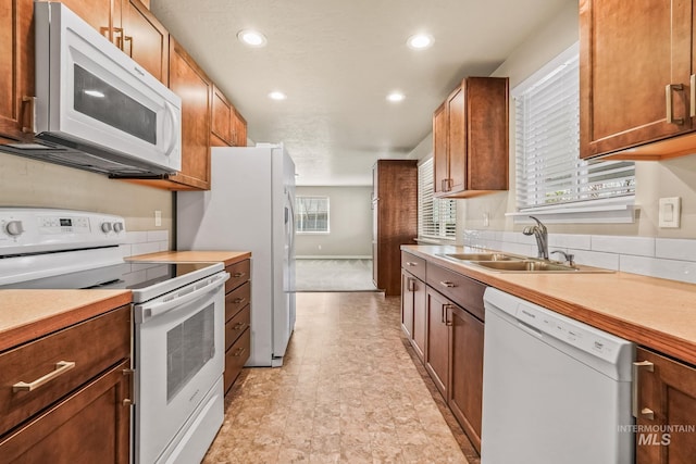 kitchen featuring light countertops, recessed lighting, brown cabinetry, white appliances, and a sink