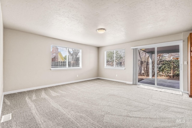 carpeted spare room with a textured ceiling and baseboards