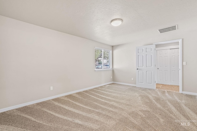 unfurnished bedroom featuring visible vents, light carpet, a textured ceiling, and baseboards