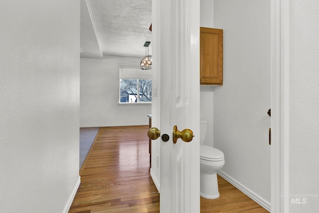 bathroom with toilet, a textured ceiling, baseboards, and wood finished floors