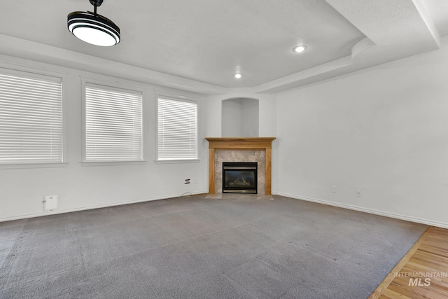 unfurnished living room featuring a tile fireplace, a raised ceiling, baseboards, and recessed lighting