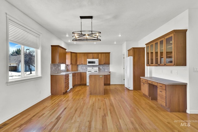 kitchen featuring white appliances, a kitchen island, glass insert cabinets, pendant lighting, and built in desk