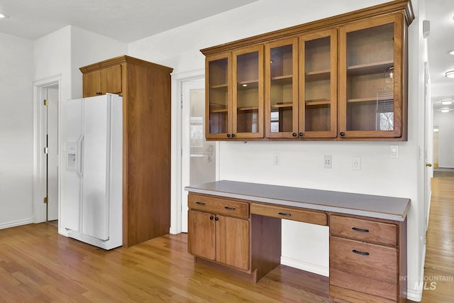 kitchen with glass insert cabinets, white refrigerator with ice dispenser, brown cabinets, and light wood-style flooring