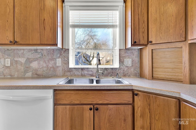 kitchen with white dishwasher, a sink, light countertops, backsplash, and brown cabinetry