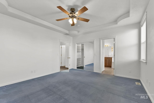 unfurnished bedroom with ensuite bathroom, visible vents, baseboards, dark carpet, and a raised ceiling