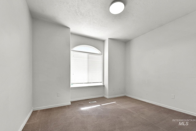 carpeted empty room with visible vents, baseboards, and a textured ceiling