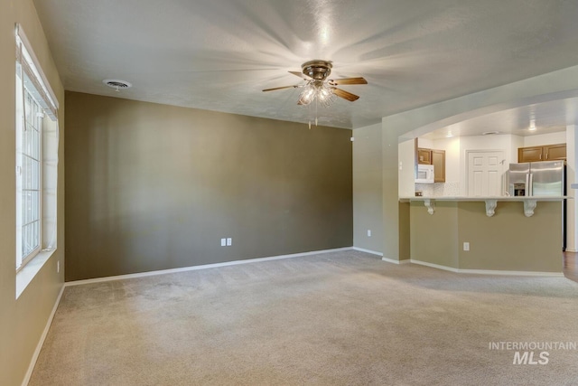 4935 N Rathbone Ave, Meridian, ID 83646 - unfurnished living room with a ceiling fan, light colored carpet, healthy amount of natural light, and arched walkways